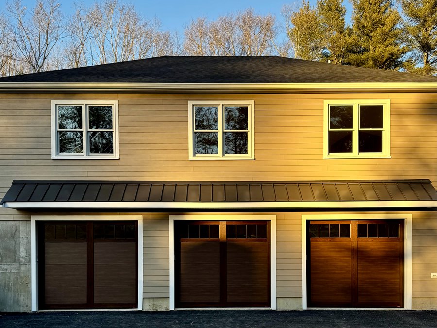 Three wood look carriage doors under a standing seam awning in evening light