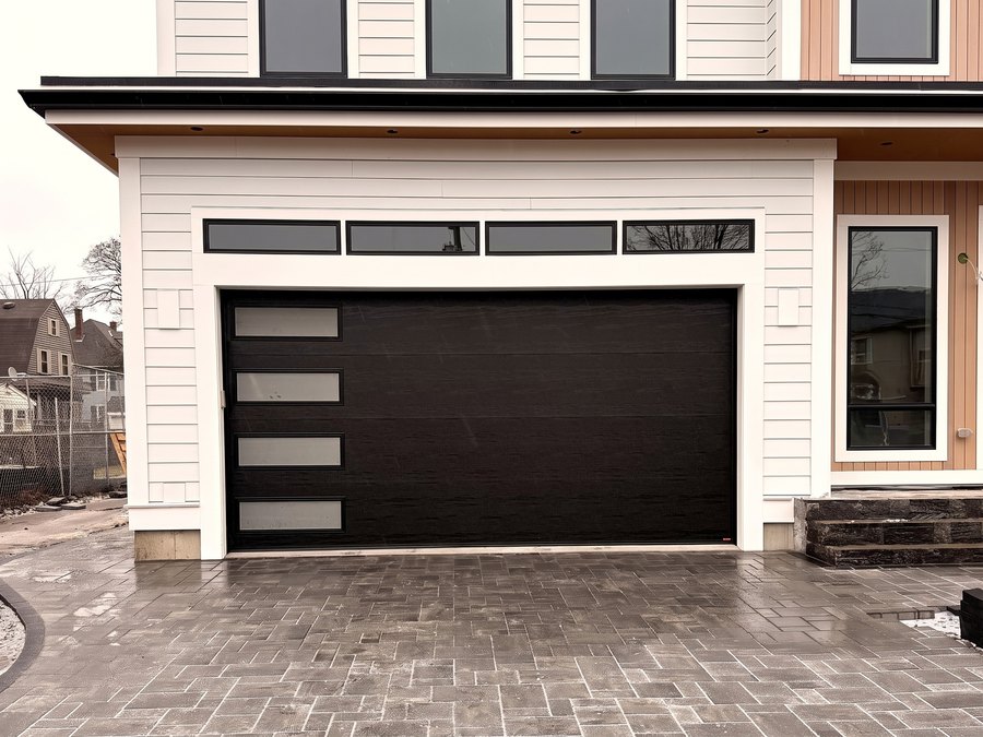 Flat black modern garage door with four vertical lites, on a new build with a paver driveway